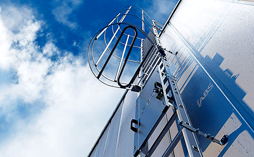 Metalen trap met rugbescherming op een gevel van een gebouw, gefotografeerd vanuit kikkerperspectief tegen een blauwe lucht met wolken.
