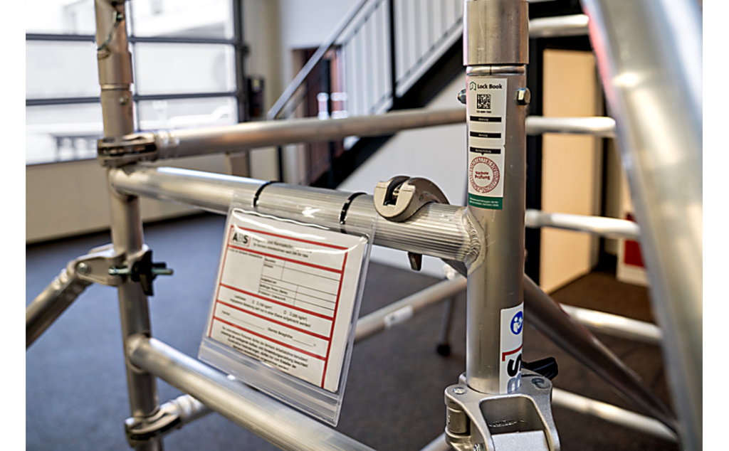 Close-up van een mobiel hefwerkplatform. Er is een goedkeurings- en etiketteerplaatje en een testzegel te zien. Dit voorbeeld is representatief voor de hele productserie.